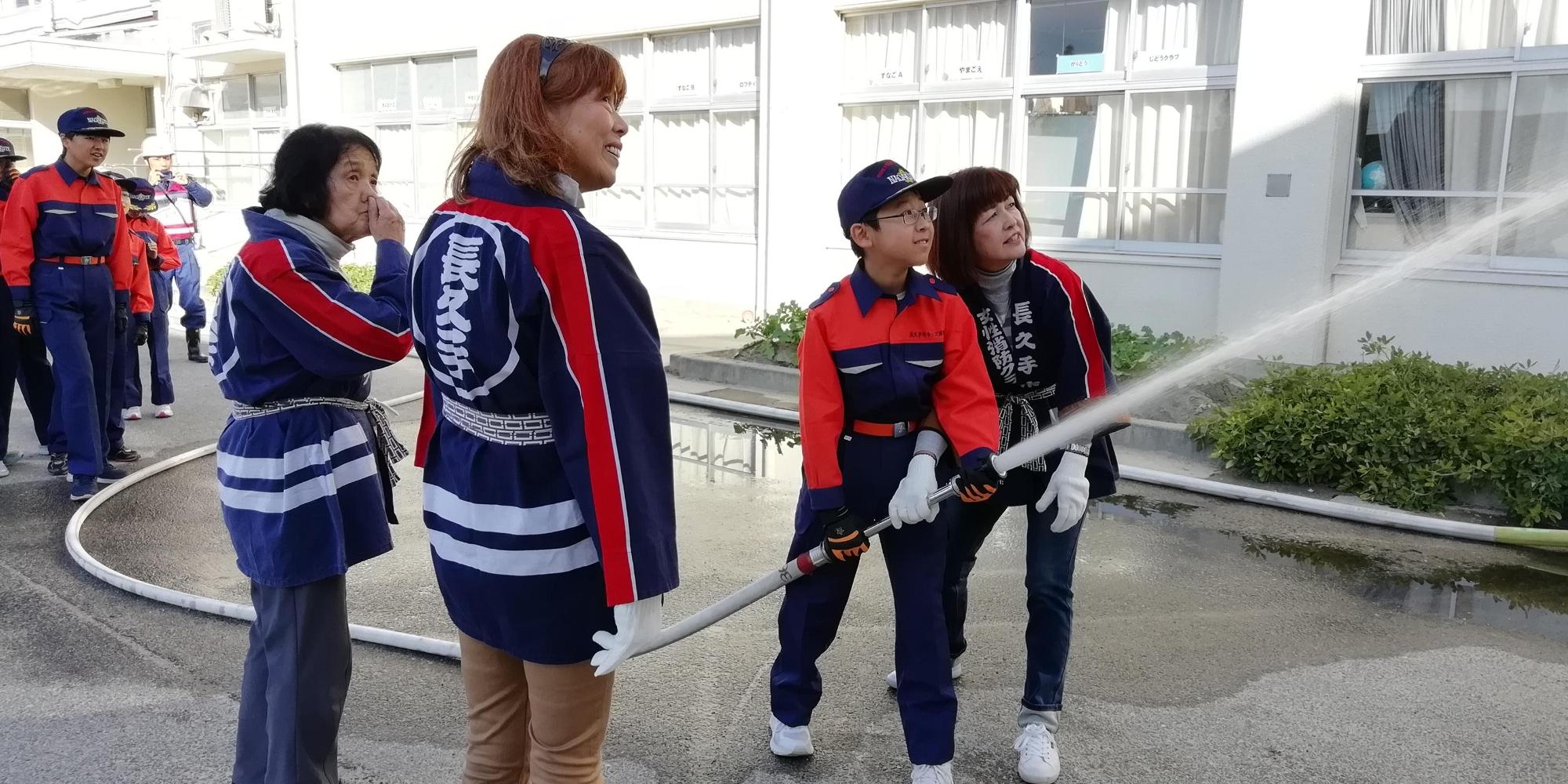 法被姿の長久手市女性消防クラブ員と一緒にキッズ消防団員が放水体験をしている写真