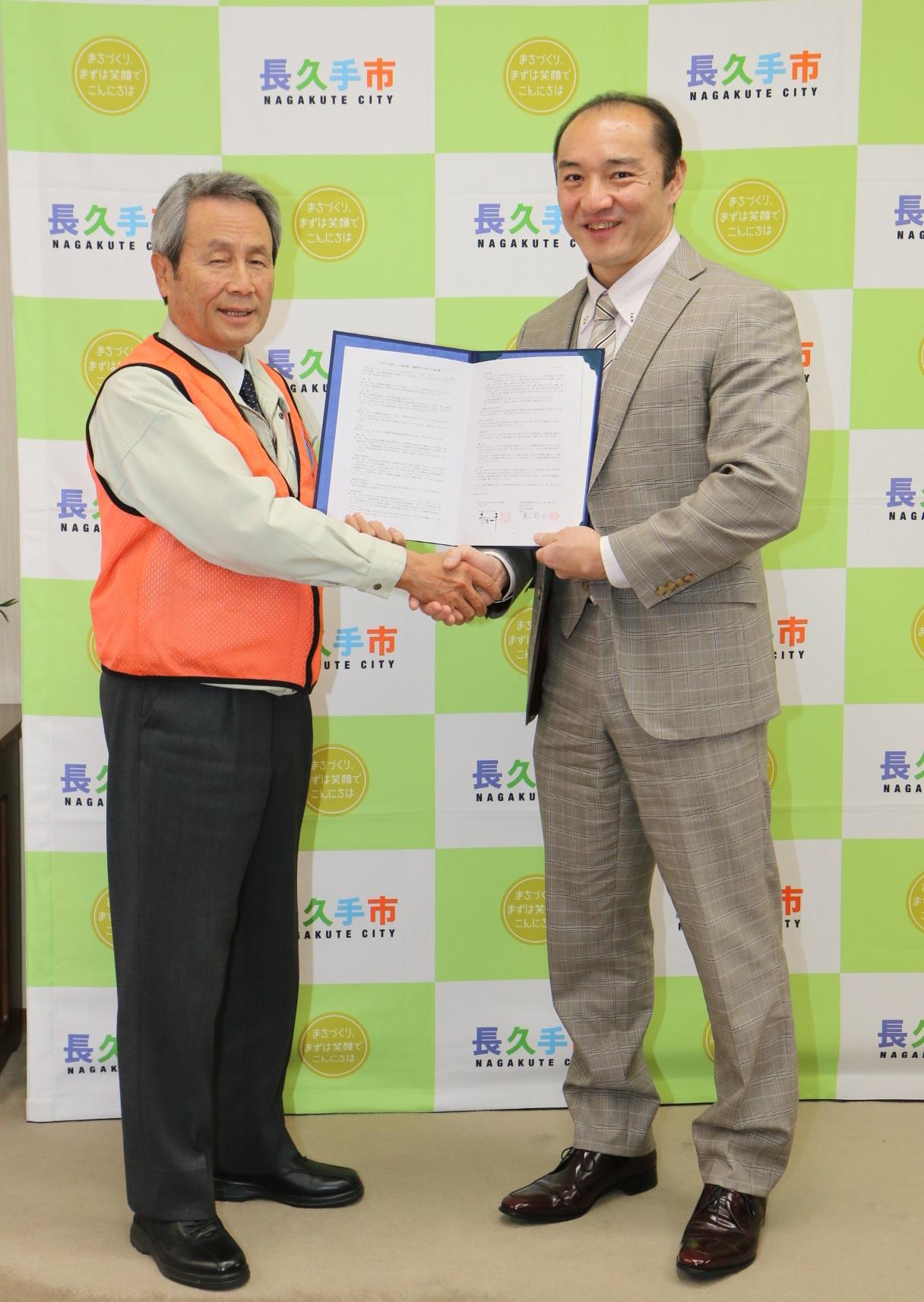 株式会社 ゼンリンの関係者の男性と市長が左手で協定書を広げて見せ、右手でしっかり握手をして写っている写真