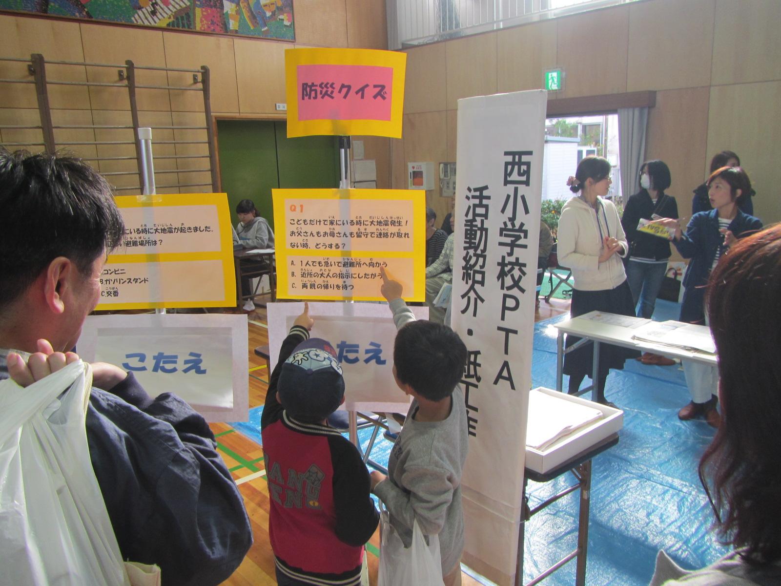 体育館に掲示されている防災クイズの方を子供たちが指し示している様子を後ろから保護者が見ている写真