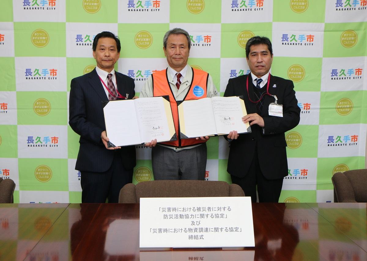 協定式にて3名の関係者が2つの締結書を一緒に持ち記念撮影をしている写真