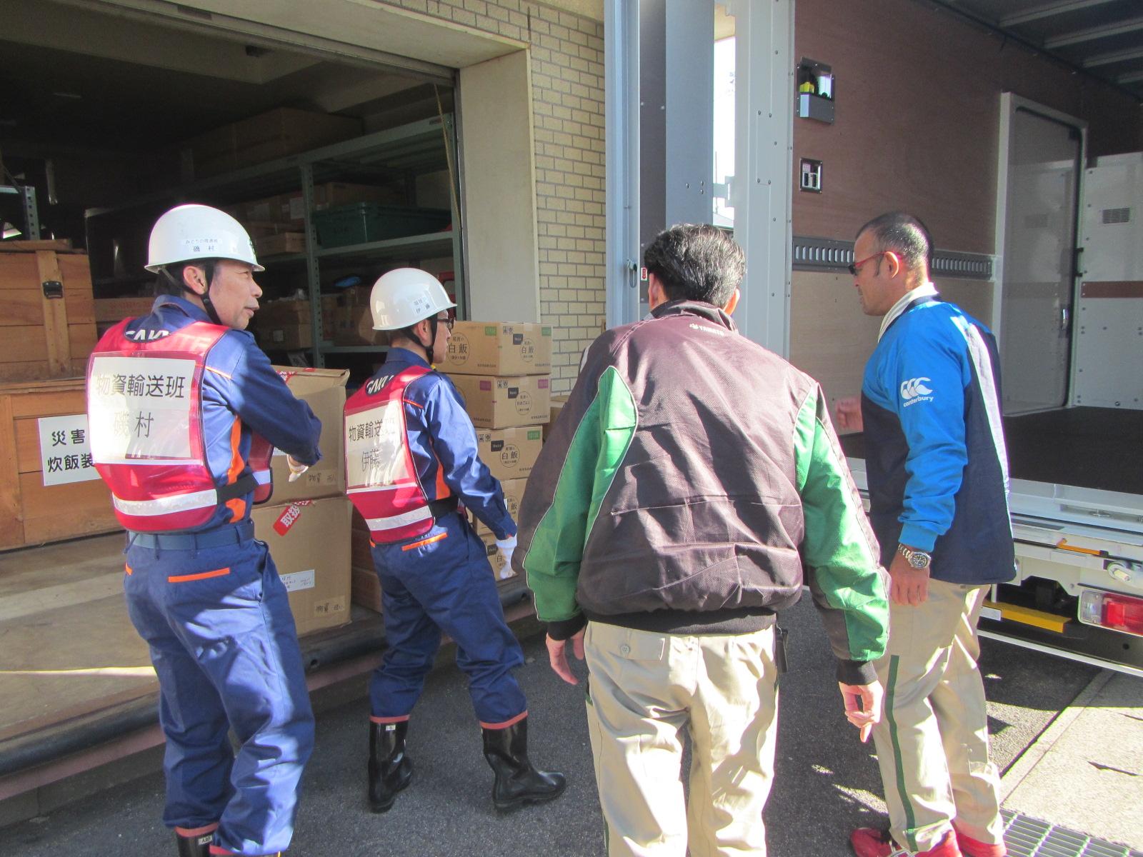 2名の男性と2名のヘルメットを被った男性が段ボールの前で話し合いをしている写真