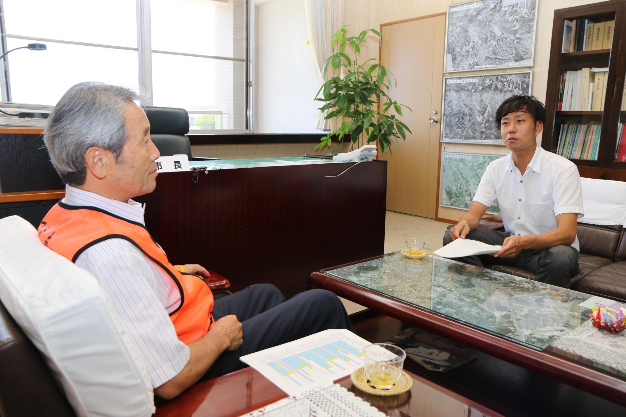 市長と職員の男性が応接室の椅子に向かい合って座って話をしている写真