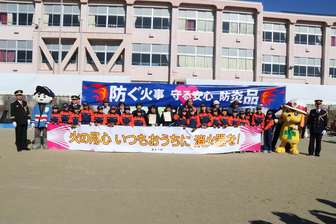 表彰状を持った標語川柳受賞者2名を中央にキッズ消防団たちが標語川柳広報幕を持って記念撮影している写真