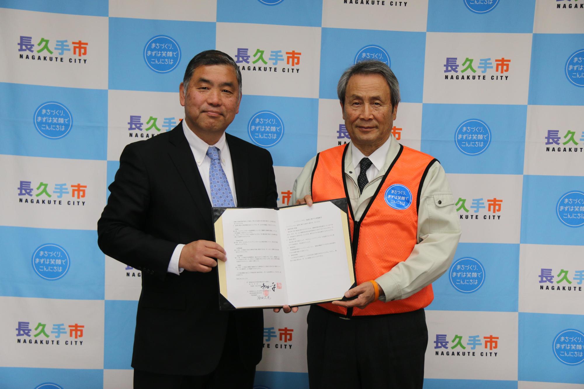 締結式で協定書を一緒に持ち記念撮影をしている関係者2人の写真