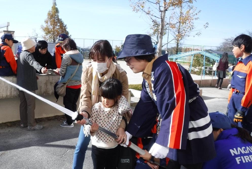 女性消防クラブの方と一緒にお母さんと女の子がホースを持って放水している写真