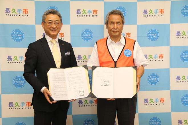 男性二人がそれぞれ協定書を開いて持っている協定締結式の様子の写真