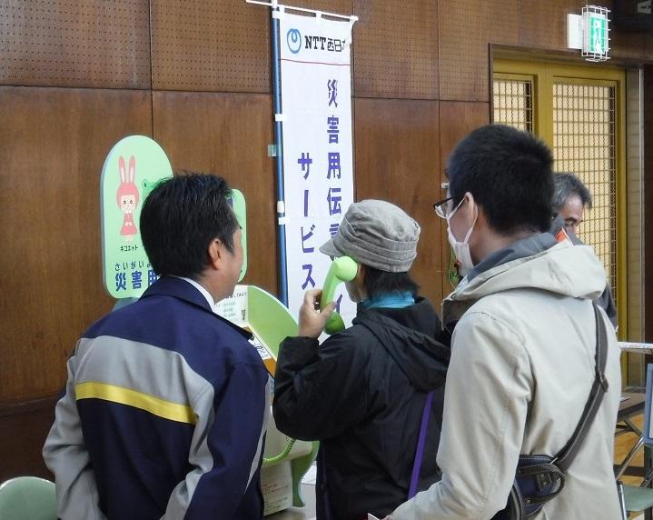 灰色の帽子を被った人が緑の受話器を持ち伝言ダイヤルを試している写真