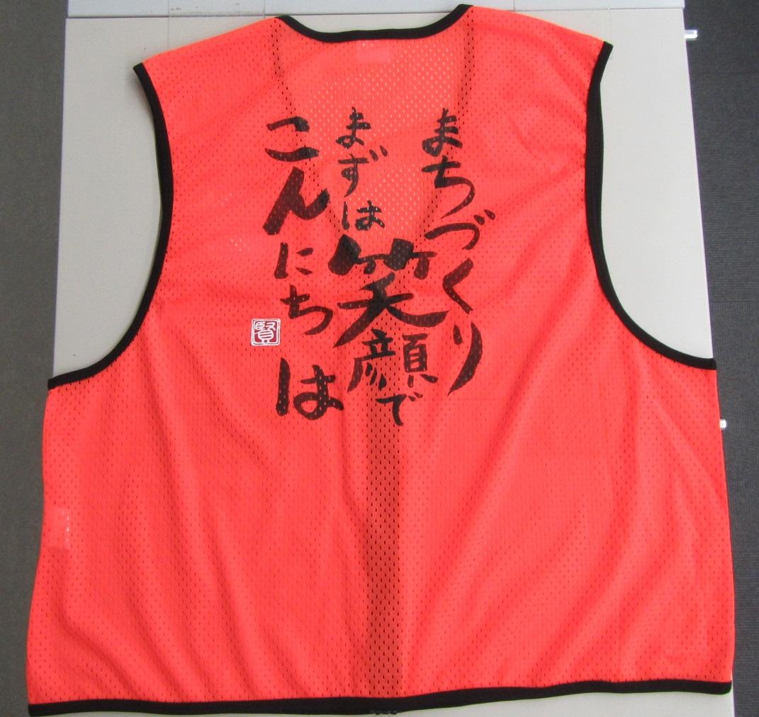 まちづくりまずは笑顔でこんにちはと書かれてあるオレンジ色のベスト後ろ側