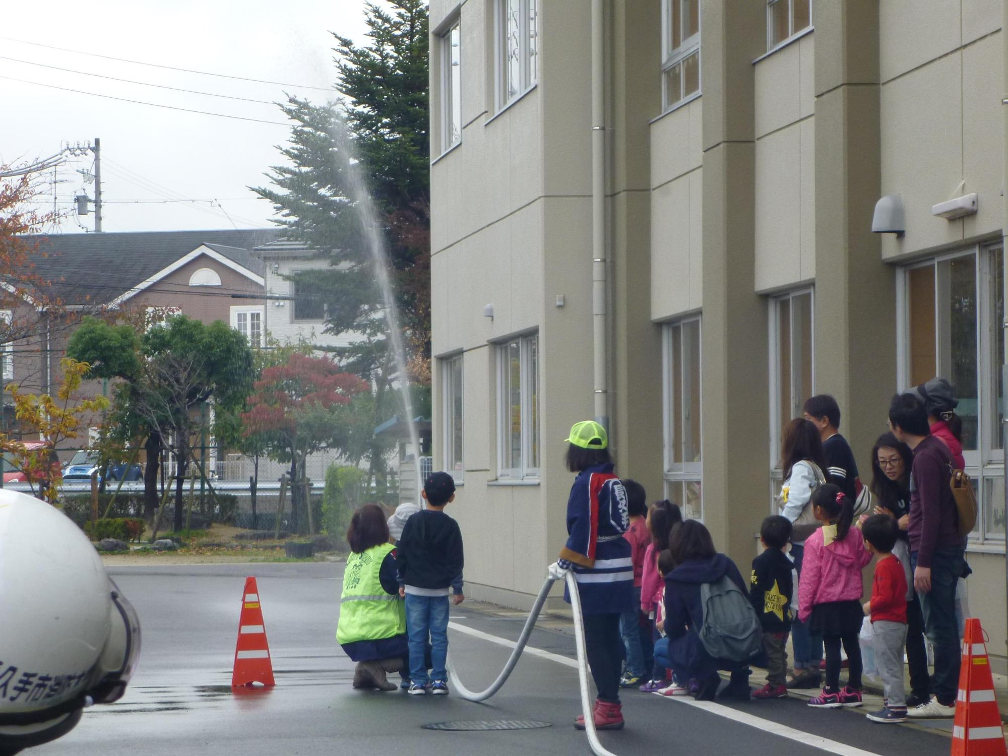 女性消防クラブの指導のもと子供たちが放水を行っている写真
