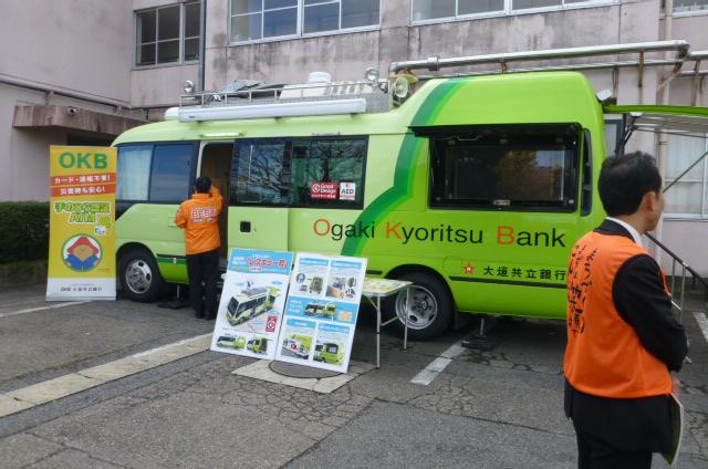 黄緑色の大垣共立銀行のレスキュー号の前にパネルが展示してあり、オレンジ色のジャンバーを着たスタッフが車の中を向いており、手前にオレンジ色のベストを着たスタッフが立っている写真