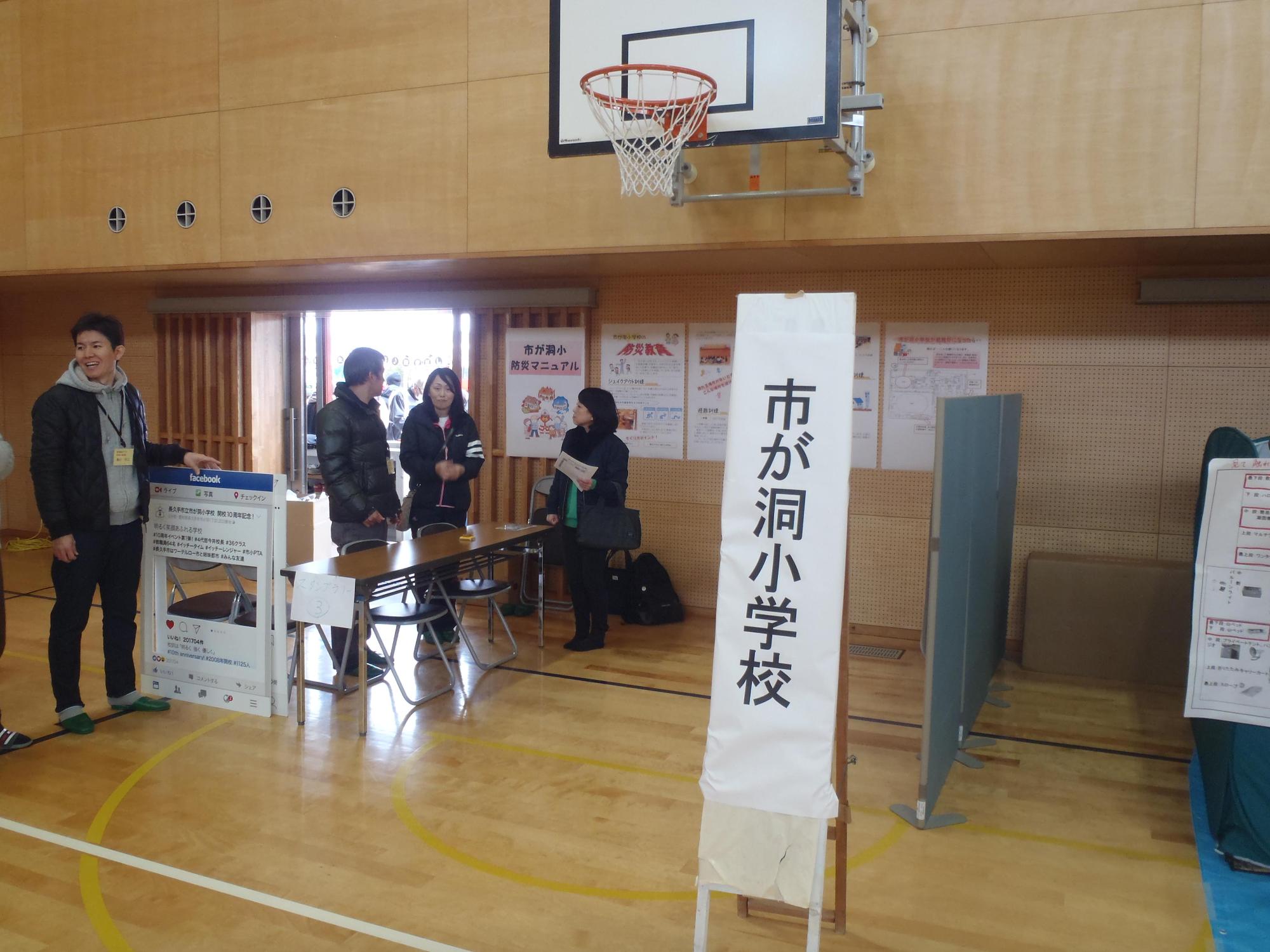 体育館にて、市が洞小学校による防災マニュアル等のパネル展示が行われており、スタッフ同士が話をしている写真