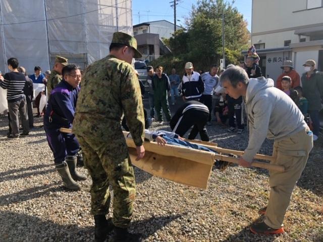 参加者たちが自衛隊員のアドバイスを受けながら子供を担架に乗せて運ぼうとしている写真