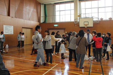体育館の中で、大勢の参加者がスタッフに教わりながら三角巾を使った応急手当訓練を行っている写真
