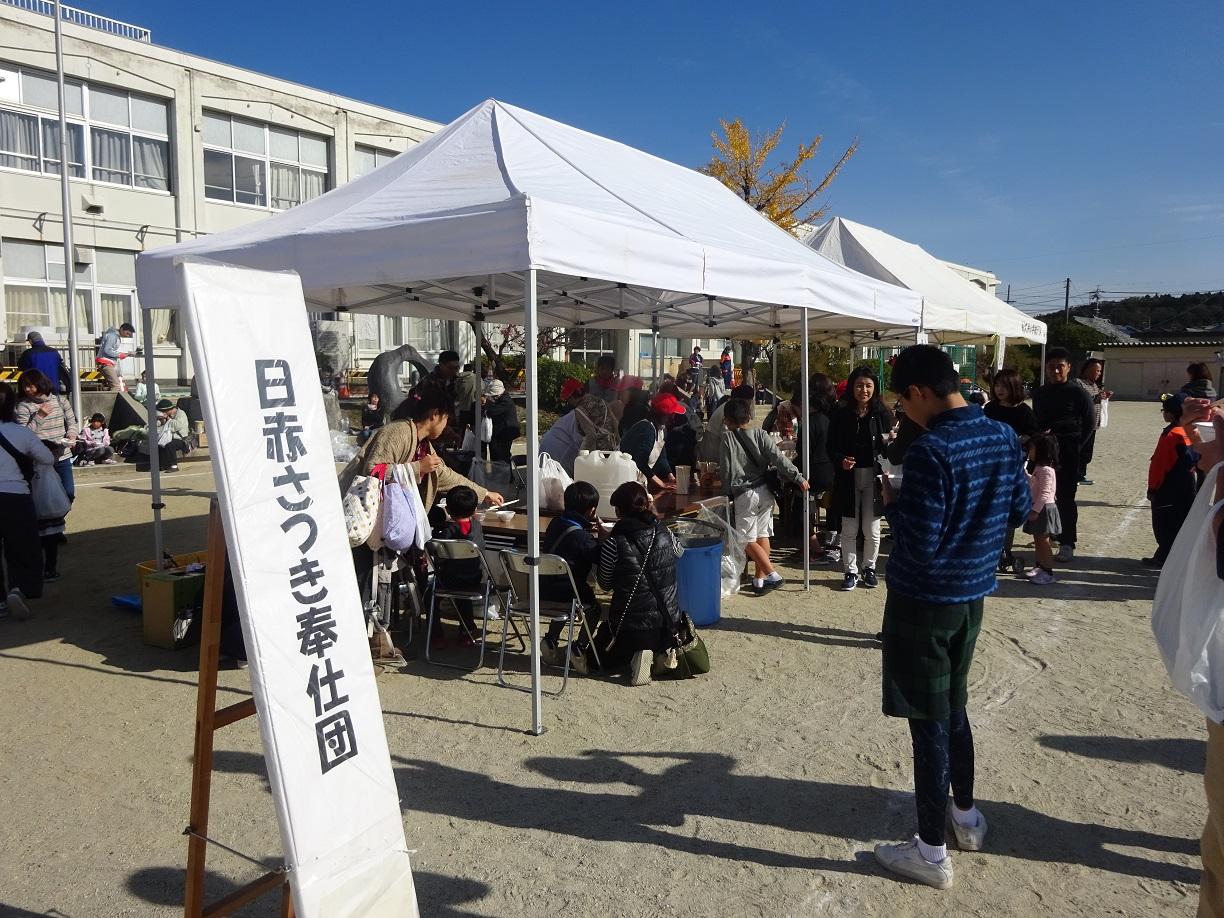 日赤さつき奉仕団と書かれた看板の横にテントが張られ、テントの中では炊き出しを食べている人たちの写真