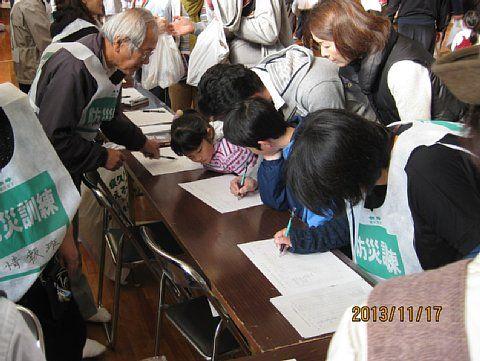 多くの訓練の参加者が、長机の上に置かれた用紙に記入している受付の訓練の写真