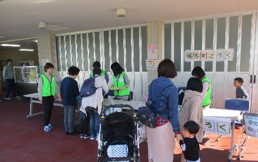 緑のお揃いのジャンバーを着た関係者の人に話を聞いている女性と順番を待っている親子づれの写真