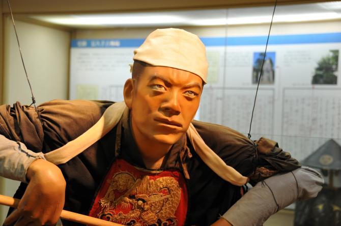 頭に白い布を巻き険しい表情をしている人形の展示物の写真