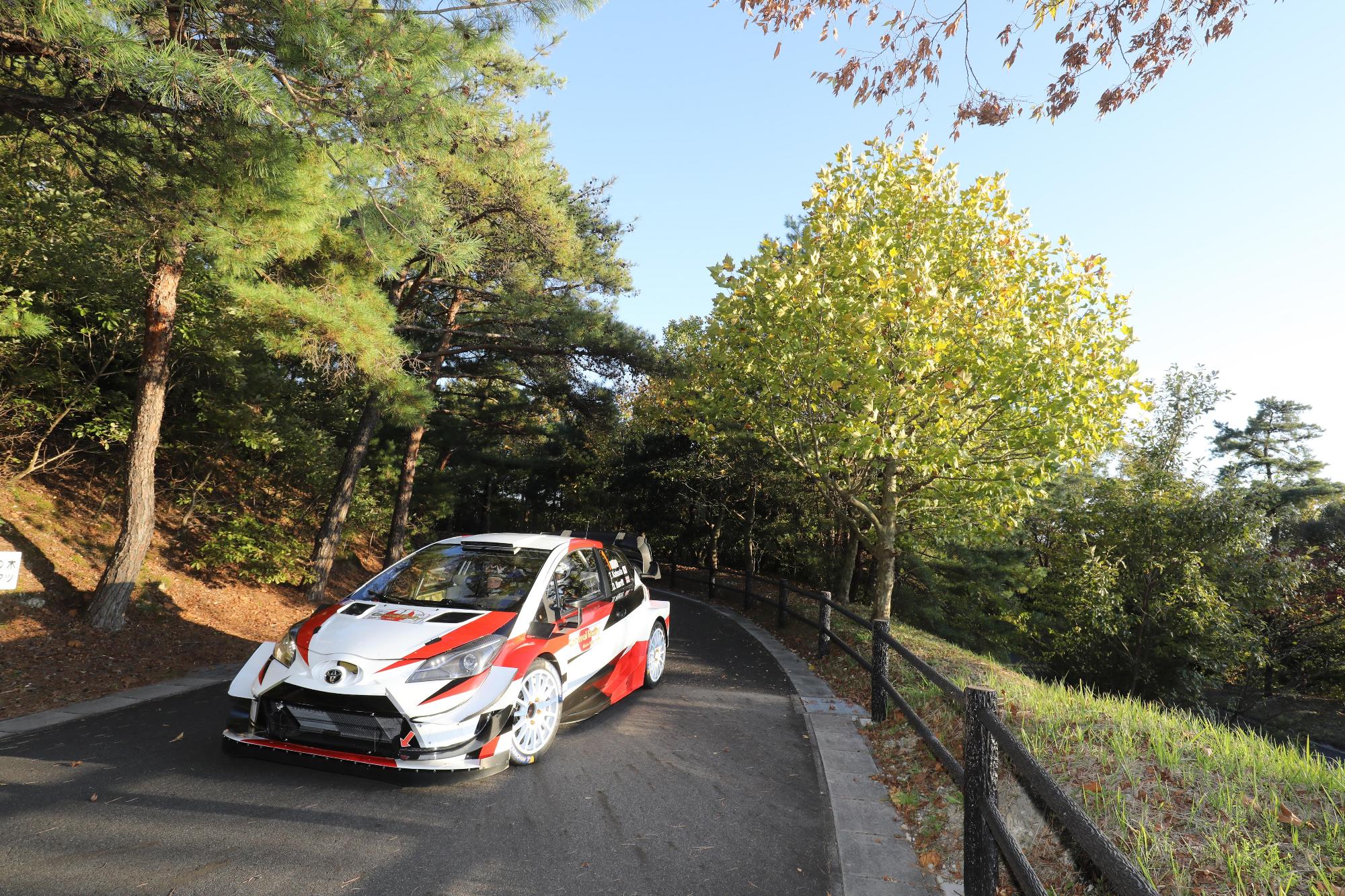 白い車体に赤と黒色が入っているラリーカー(車)が山道のコースを走っている写真