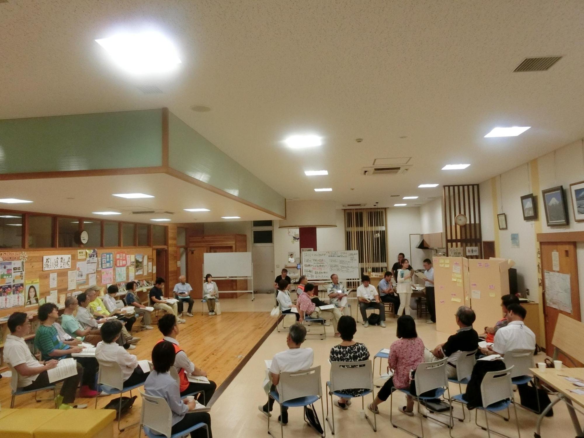 市民の人達がたくさん集まりいすに座り話し合いをしている写真