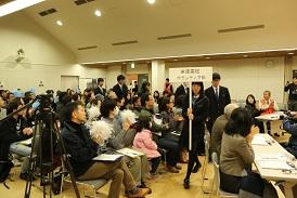 プラカードを女子生徒が持って、その後ろに選手が続いて客席の間を歩いて入場している写真