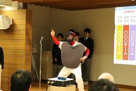野球のユニフォームを着てマスクとプロテクターを身に着けた審判長が、両足を肩幅に広げ、右手の人差し指を上に挙げて合図をしている写真