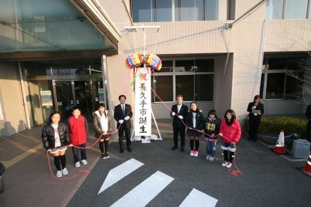 中央に「長久手市誕生」の垂れ幕が下がったくす玉、その両脇でくす玉の紐をもって立っている長久手小学校の児童と市長の写真