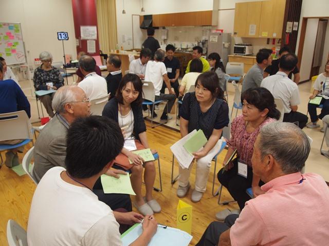 グループに分かれて、円を作って椅子に座っており、白髪の年配の男性の話を同じグループの方々が聞き入っている様子の写真