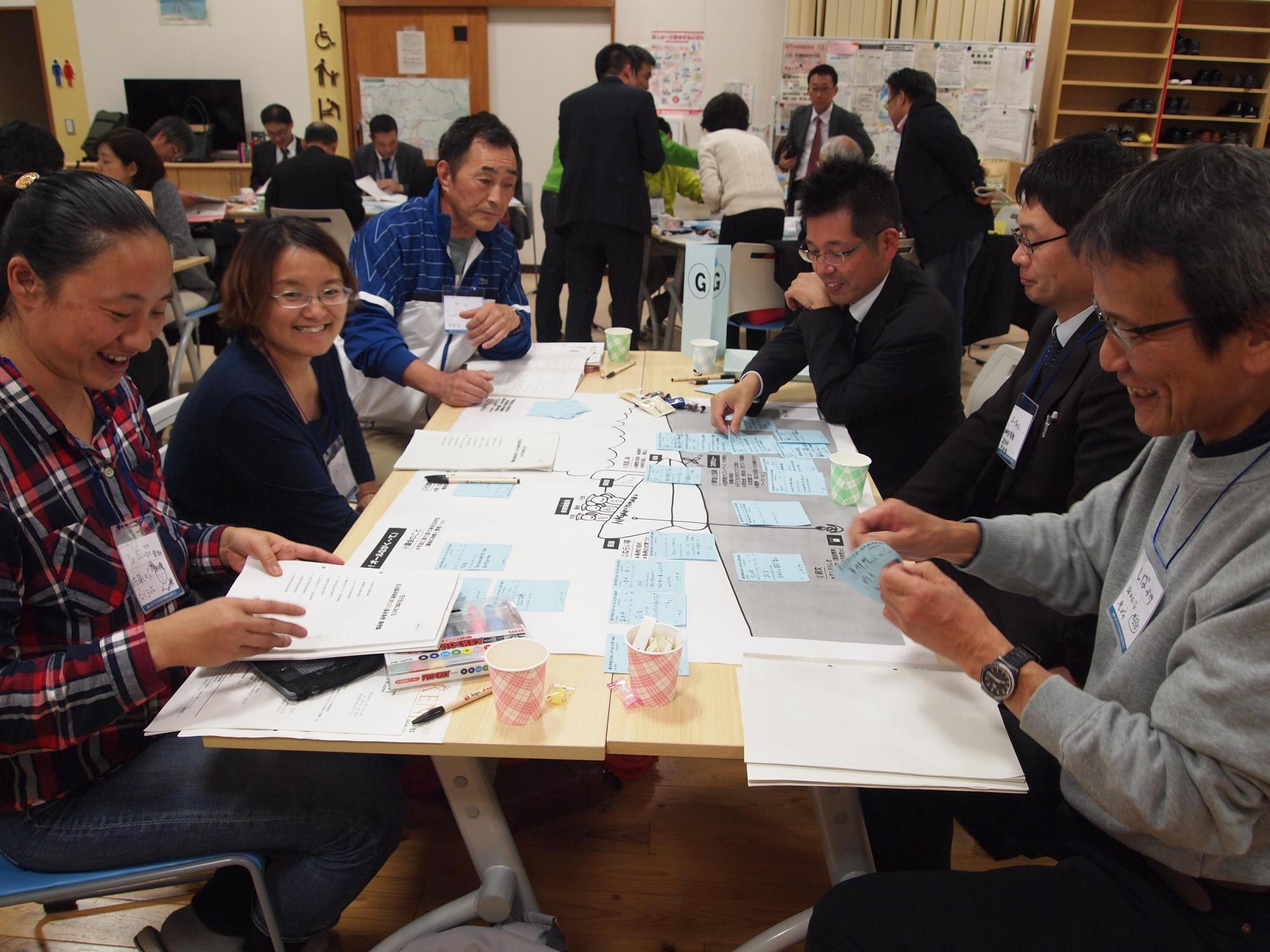 グループに分かれて話し合いが行われており、グループの皆さんが机に置かれた資料に目を通しながら笑顔で話し合いをしている写真