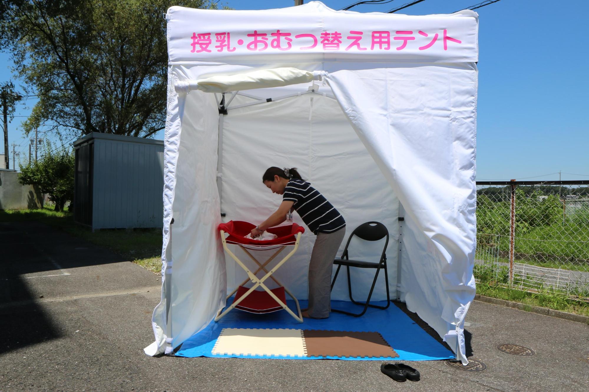 地面にブルーシートが敷かれ、パイプ椅子、おむつ交換台が設置されてある移動式赤ちゃんの駅テント内の写真