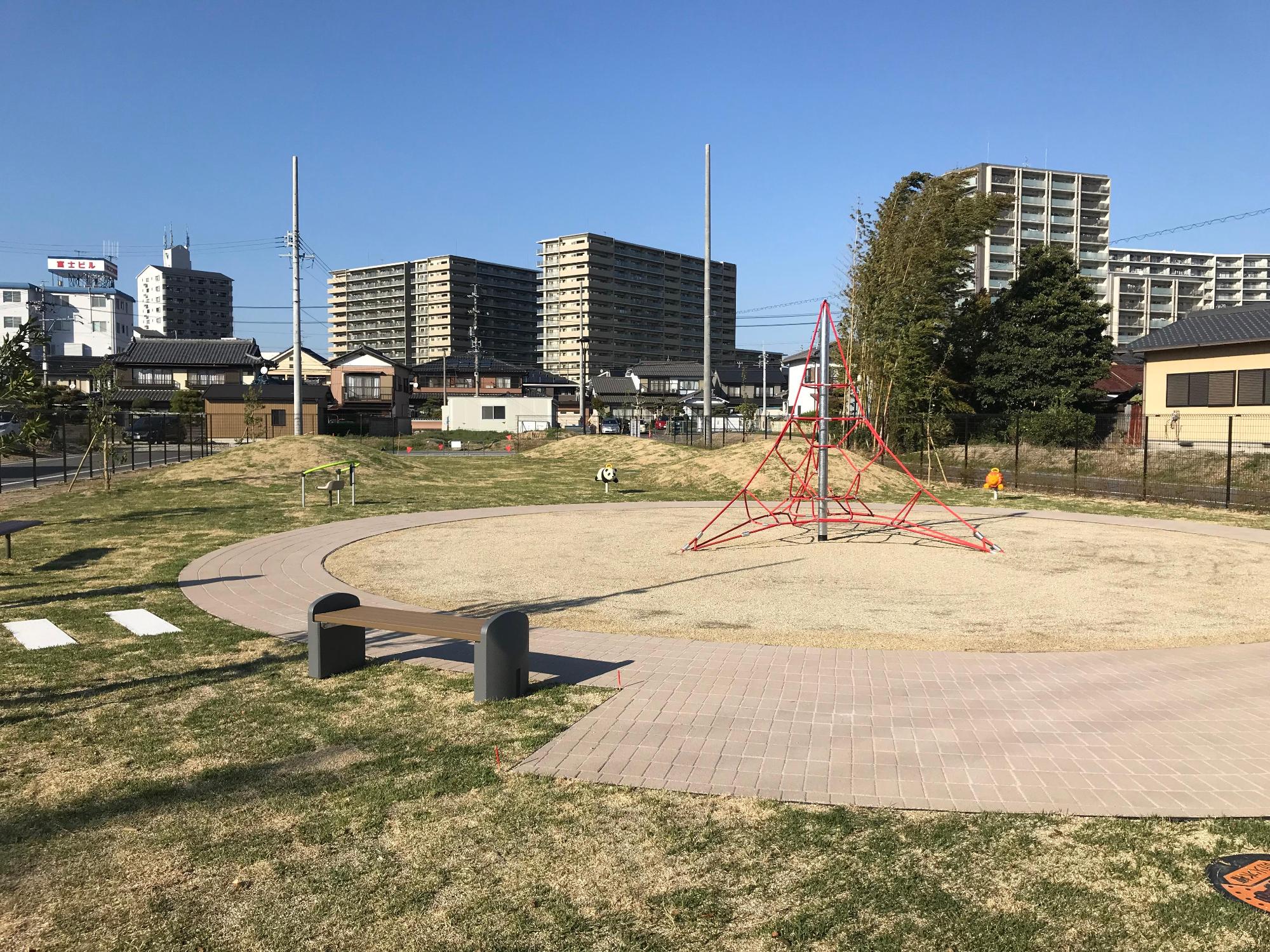 奥に数棟のビルが建っているのが見え、中央にロープジャングルジムが設置されてある下山(しもやま)公園の写真