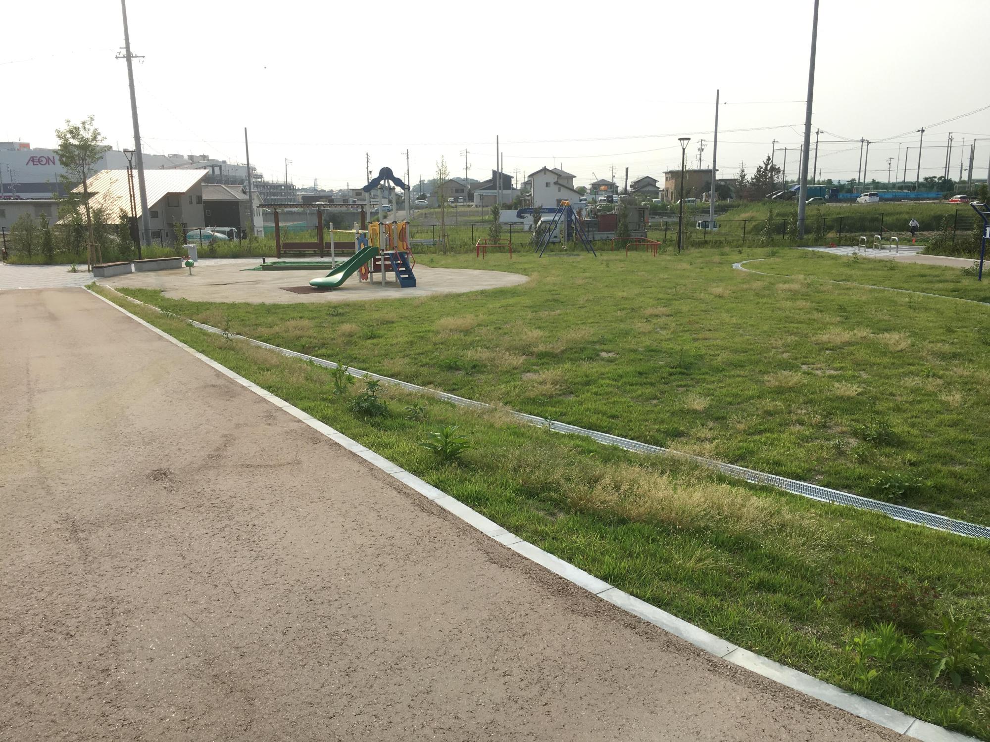 手前に歩道、その横に芝生が植えられた広いスペースがあり、一角に遊具が設置されてある長久手中央3号(ながくてちゅうおうさんごう)公園の写真