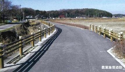 農業集落道の両脇にフェンスが設置されてあり、遠くには畑や住宅が写っている写真