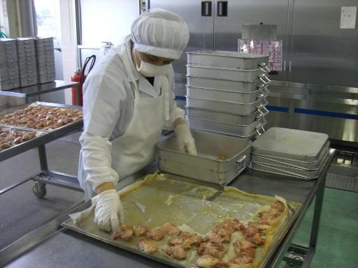 白色の作業着に帽子を被ったスタッフが、天板に並んだ鶏肉をバットに移し替えている写真