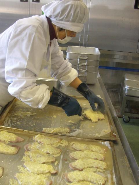 白い作業着を着たスタッフが、焼きあがった豚肉をバットに詰め替えている写真
