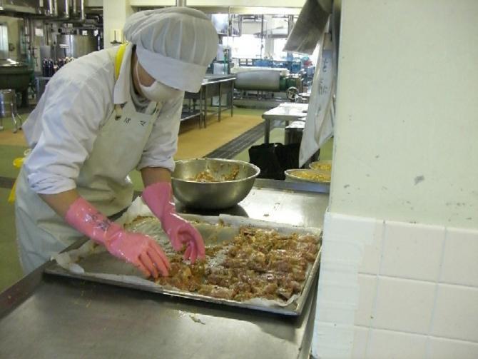 白色の作業着にエプロンを着用したスタッフが、バットに鶏肉を並べている写真