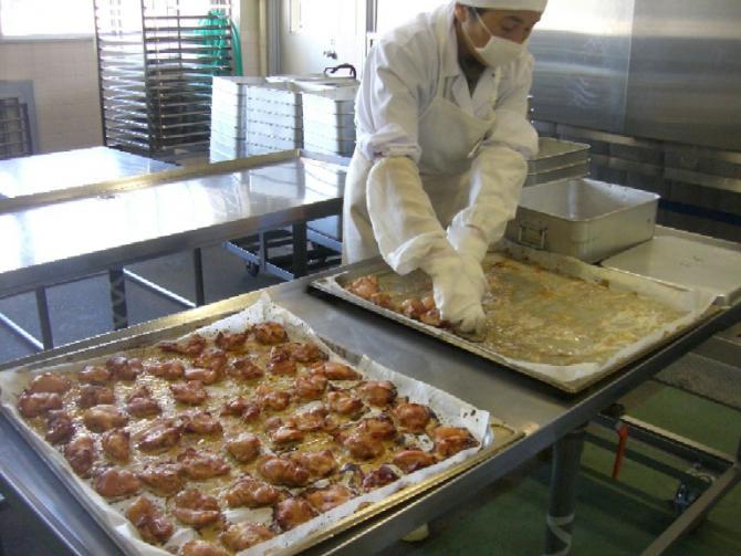 白色の作業着を着たスタッフが、こんがり焼きあがった鶏肉をバットに移し替えている写真