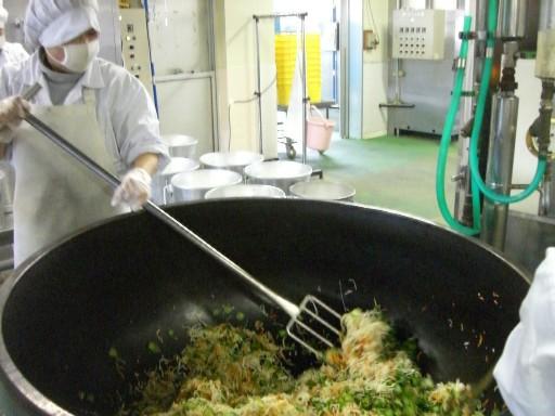 白い作業着を着ているスタッフ2人が、大きな釜に入れた材料をかき混ぜている写真