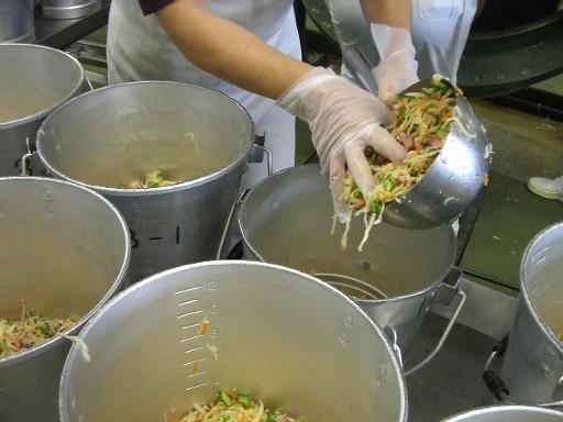 スタッフがたくさんの食缶に大きなおたまを使って注ぎ分けている写真