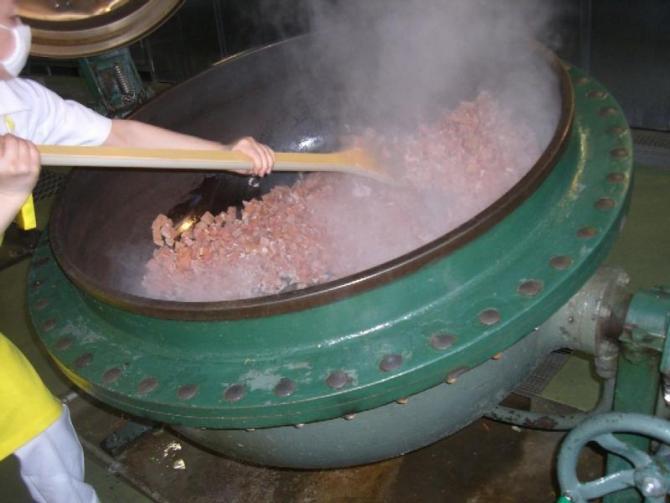 大きな釜に鶏肉や大豆、野菜などを入れて大きなヘラでかき混ぜている写真