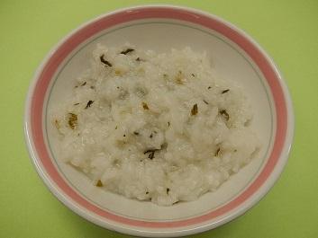 薄いピンク色に縁どられた白色の器に、七草と米を混ぜて炊いた七草がゆを盛り付けた写真