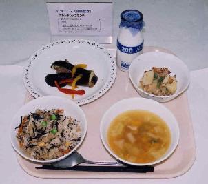 給食トレーの上に、長久手の豆ごはん、牛乳瓶、なすと思ったらハンバーグ、ベルギーのリエージュ風サラダ、かぼちゃのスープが盛りつけられた写真