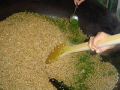 大きな釜の中に入れた大豆と落花生に、おたまで青のりを振りかけながらかき混ぜている写真
