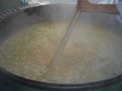大きな釜で材料を煮込んでいるのをスタッフが、かき混ぜている写真