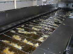 横長のフライヤーの油の中で、大量のいわしが揚げられている写真