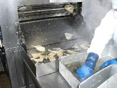 白い作業着を着たスタッフが、フライヤーから出てきたきつね色に揚がったいわしをタレにからめている写真
