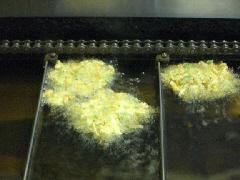フライヤーの油にこんがりときつね色に揚がっているかき揚げの写真