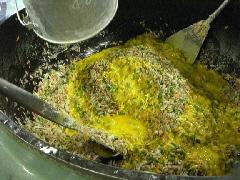 大きな釜で混ぜ合わせた材料に溶き卵を投入している写真