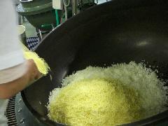 白い作業着を着たスタッフが、大きな釜に入れたたまねぎにチーズを投入している写真