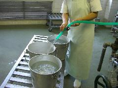 材料で使用する分の水を、3つの食缶にホースで入れている写真