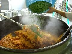 大きな釜で炊き上がったチキンライスに大量のグリンピースを入れている写真